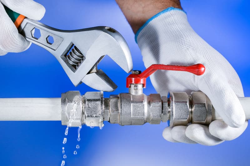 Een hand die een rode hoofdkraan voor de watertoevoer dichtdraait in een meterkast om een lekkage te stoppen.